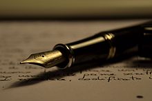 Black fountain pen with gold nub resting on sheet of paper with handwriting on it